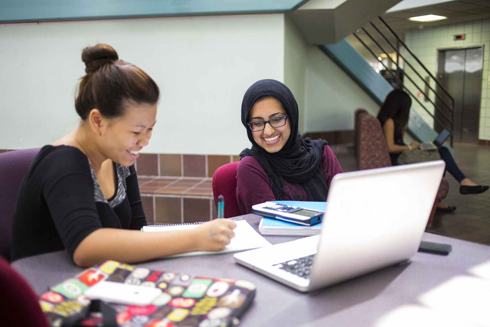 Two students studying at a table with books and laptop