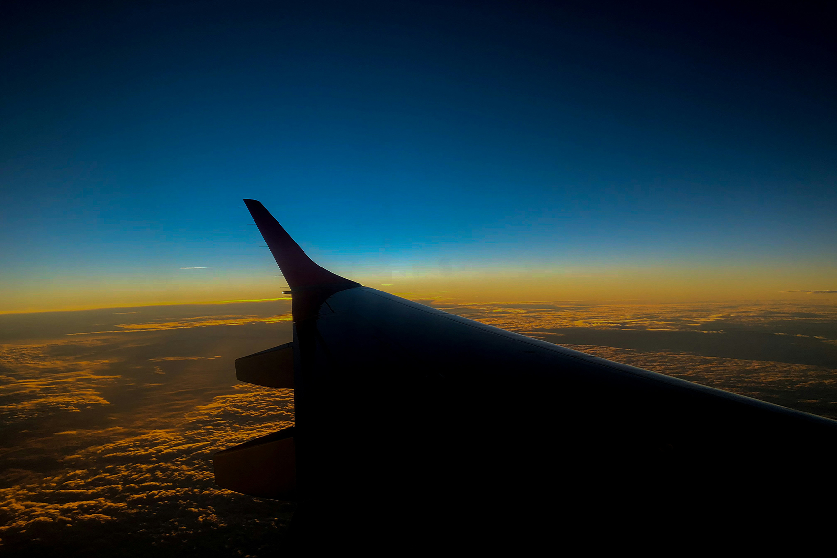 Airplane wing flying over a sunset above the clouds